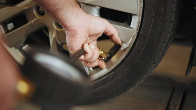Car Tire Pressure Check in the Auto Service Garage. Detail of inflating tire and checking air pressure use gauge in mechanics hands. Professional Mechanic is Working on a Car in a Car Service