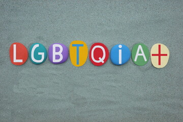 LGBTQIA Plus, creative logo composed with multi colored stone letters over green sand
