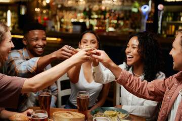 Young multiracial group of friends in casual clothing enjoying celebratory toast at restaurant