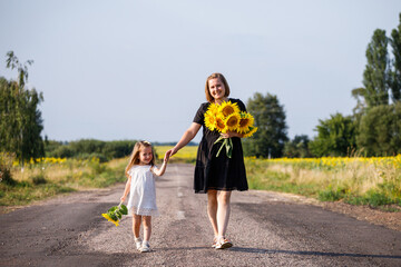 Happy childhood. Mother and child walking. Mother and child have fun in nature. A bouquet of sunflowers. Emotions of happiness
