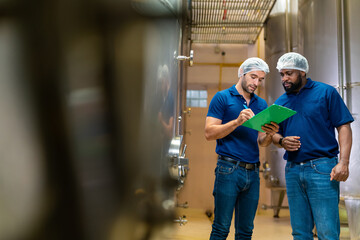 Professional male winemaker staff working and inspecting wine in modern wine cellar with stainless steel barrels. Winery manufacturing, Alcohol and wine winemaking quality control process concept.