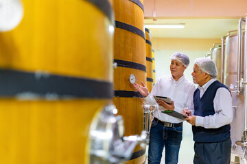 Professional Asian man winemaker working and inspecting wine quality in wine cellar with wooden...