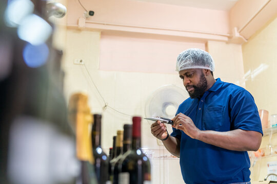 African man winemaker staff working and inspecting red wine in quality control room. Winery manufacturing, Alcohol and wine winemaking process concept.