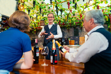 Professional senior man sommelier explaining and recommending wine to customer at wine shop or liquor store. Sommelier tasting wine in winery. Winery manufacturing industry and winemaker concept.