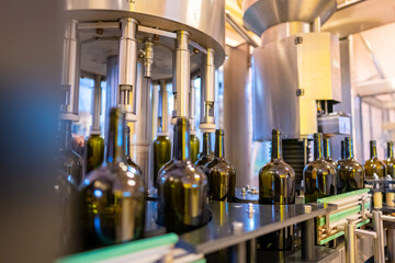 Red wine filling in the bottles by modern liquid filling machine in production conveyor line with...