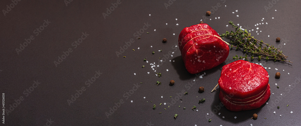 Wall mural raw ribeye steak with spices and herbs on black stone background. trendy hard light, dark shadow