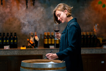 Professional woman sommelier testing red wine in wine glass with tasting and smelling at wine...