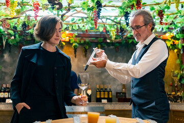 Professional senior man sommelier explaining and recommending wine to customer at wine shop or liquor store. Sommelier testing wine in winery. Winery manufacturing industry and winemaker concept.