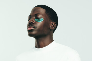 Man with melanin skin indulging in some under eye care with a hydrogel patch