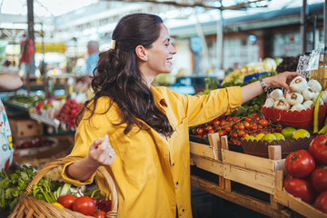 Young woman buying fresh organic produce at a local farmer's market. Picking vegetables at local...