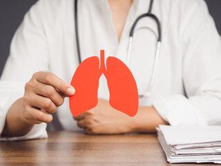 Doctor holding a lung shape symbol while sitting at a table in the hospital.