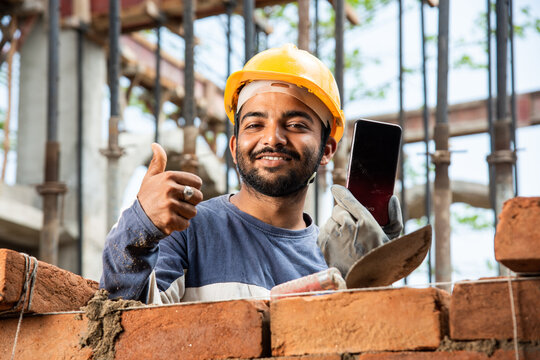 Happy smiling young indian construction labour busy on mobile phone at workplace