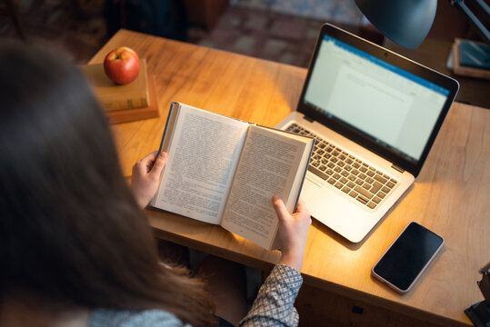 Backshot of a female student reading a book. Student reading literature, using laptop to take notes