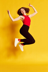 Fototapeta na wymiar Full-length portrait of young beautiful girl in casual clothes cheerfully jumping against yellow studio background. Happy and delightful. Concept of youth, human emotions, lifestyle, ad