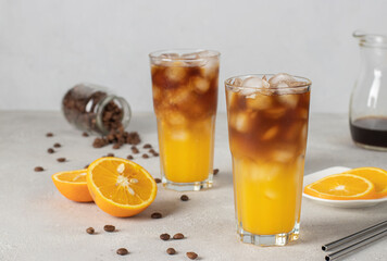 Bumble coffee with ice in two tall glass on light gray background. Espresso, orange juice and syrup in layers in transparent glasses