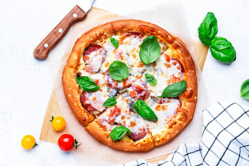 Pizza with spicy salami sausage, mozzarella cheese, tomato sauce and green basil, gray table background, top view