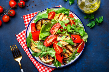 Summer healthy salad with grilled vegetables, paprika, zucchini, eggplant with cherry tomatoes and mixed herbs. Blue table background, top view