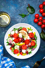 Tasty Greek salad with feta cheese, kalamata olives, tomatoes, paprika, cucumber and onion, healthy mediterranean food. Blue table background, top view