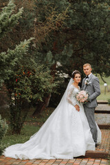 Handsome groom and charming bride together in the park. Portrait. Luxurious dress with a long train. Elegant young groom. Wedding bouquet. luxury wedding