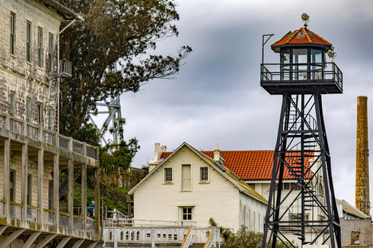 Photo of barracks and watchtower of the federal prison on Alcatraz Island of the United States of America in the bay of San Francisco, California, USA. Surveillance under a cloudy sky. Jail concept.