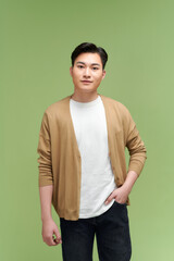 Photo of cheerful young asian guy hands pockets  isolated on green background