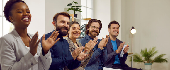Happy business audience applauding speaker after presentation at business conference. Group of happy diverse people sitting in row in office, looking away, smiling and clapping hands all together