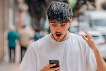 young man in the street with mobile or cell phone and expression of surprise