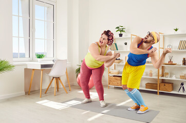 Fototapeta na wymiar Two funny people enjoying sports workout at home. Happy fat woman dancing together with personal fitness trainer. Cheerful family couple add physical activity in life and do aerobics exercise to music