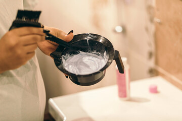 The process of preparing for hair coloring at home. Female hands with oxidizing in plastic bowl with prepared hair dye.