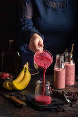A woman pours a berry-banana smoothie into a jar. Dark and moody image - 613156870