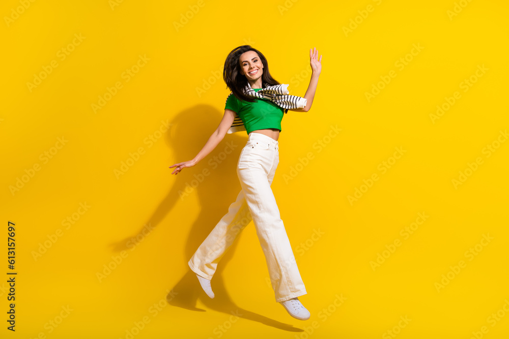 Sticker Full length photo of excited friendly lady wear white trousers jumping high walking waving arm isolated yellow color background