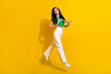 Fototapeta na wymiar Full length photo of shiny excited lady wear white pants jumping high tying sweater empty space isolated yellow color background