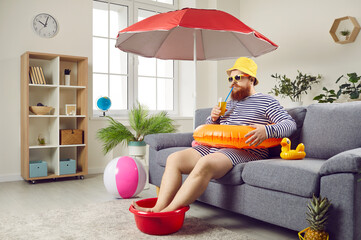 Funny redbeard Caucasian man in clothes for summer tourism with inflatable ring drinks cocktail and...