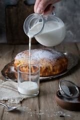 Pouring milk into a glass cup and homemade pie on a wooden table