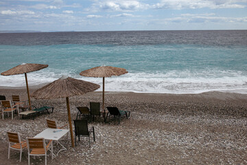 A tranquil beach scene with parasol, chair, and thatched umbrella