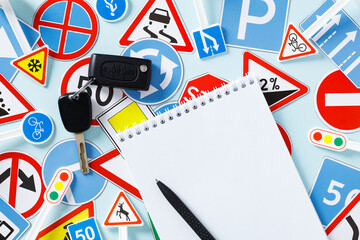 Driving school test concept. Blank paper notebook, car keys, road signs and traffic symbols on color background.
