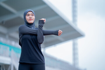 A young asian Muslim woman wearing a black hijab is exercising and running at an outdoor stadium in the morning. Modern Muslim woman concept,  Muslim woman sport concept, Islam
