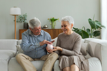 Saving money investment for future. Senior adult mature couple holding piggy bank putting money...