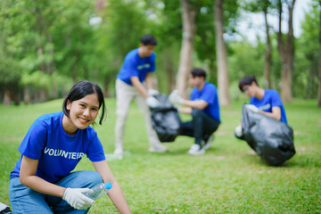 Naklejka premium Multiethnic volunteers donate their time holding black garbage bags to collect plastic waste for recycling to reduce pollution in a public park.