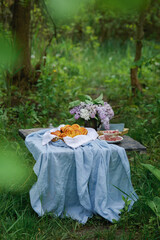 Homemade fresh sugar buns, a bouquet of lilacs and books and vintage cup on a table in the garden - 613165411