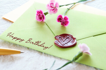 Envelope wax seal with carnation flowers on white table. Self made low impact greeting card.