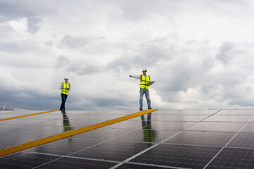 Two young Asian engineers checking the installation of solar panels on the factory roof, checking the installation of solar panels against the drawings in the computer.