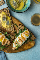 Swedish meal. Crisp breads with different toppings : pickled herring in mustard sauce, egg, arugula and cod roe paste, juice and coffee on blue background.