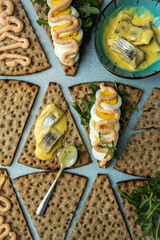 Assortment of crisp bread open sandwiches with pickled herring and egg-arugula- cod roe paste toppings and bowl with pickled herring in mustard sauce.