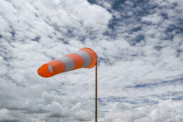 Orange-white windsock against the blue sky in sunny weather. Wind vane indicates the strength and...
