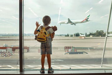 Child, watching from the window of the airport the planes, taking off and landing while waiting at  to board the aircraft - obrazy, fototapety, plakaty