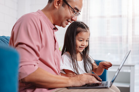 Cute Little Asian Daughter With Father Working On Laptop At Home. Single Loving Dad Man Shopping Insurance To Daughter By Online Technology.