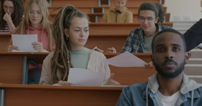 Group of students getting examination papers from teacher writing exam thinking concentrated on education in classroom. People and knowledge assessment concept.