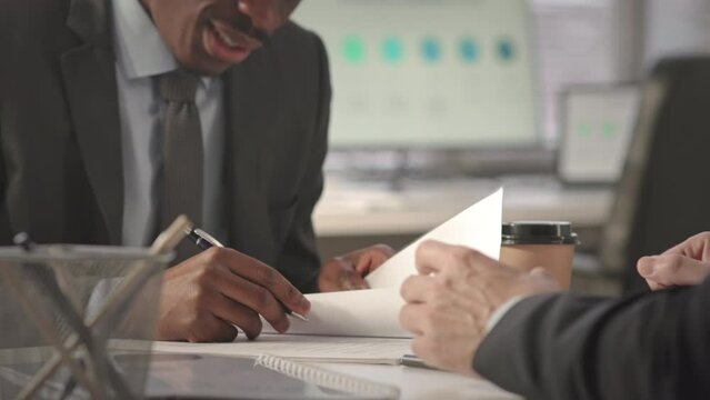Cropped shot of African American businessman in suit signing contract while having office meeting with business partner