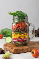 Healthy salad with quinoa, cucumbers, corn, cherry tomato, radish, spinach, lettuce and olive oil in a Mason jar